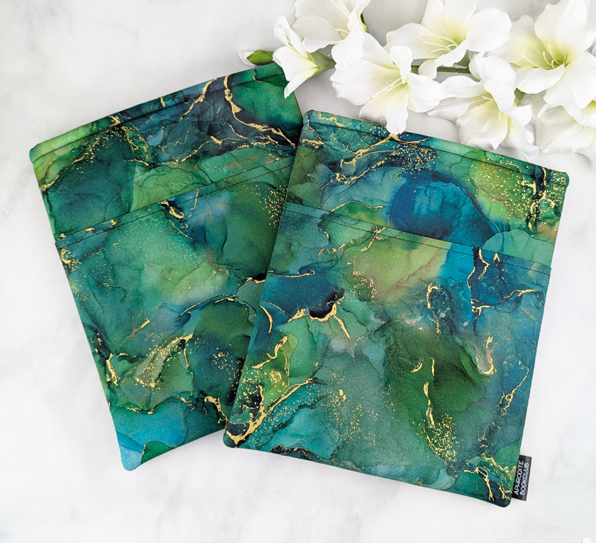 two large padded book sleeves with pocket. fabric showcases green and teal marble texture with gold accents.