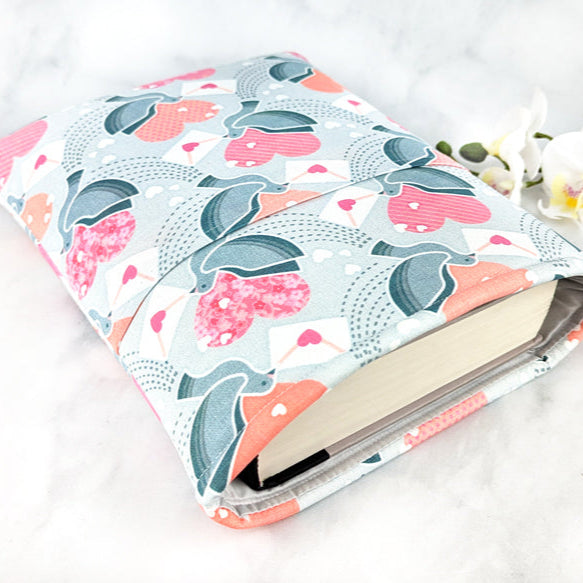Book sleeve with a soft grey background featuring white doves holding envelopes with pink hearts, surrounded by pink and red heart shapes and dotted trails.