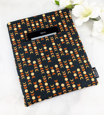 large padded book sleeve with pocket. fabric showcases moon phases in beige and orange shades on a dark navy background.