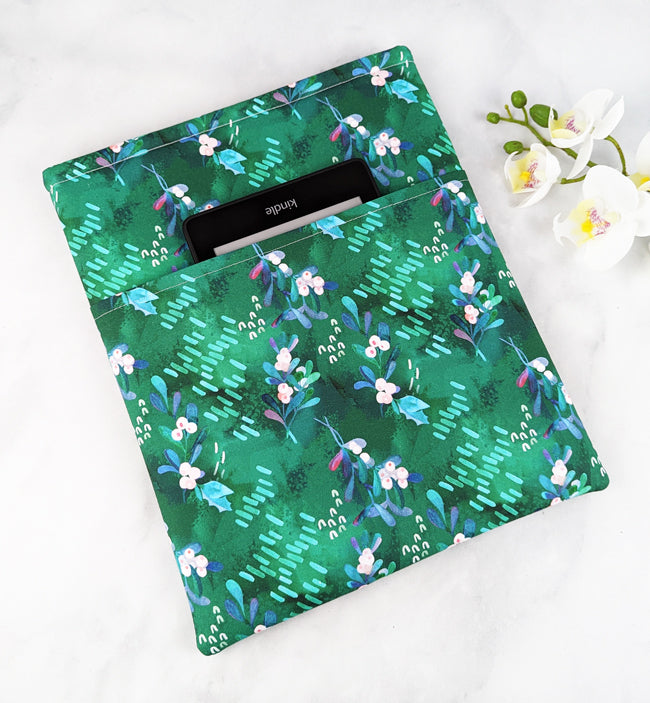 Green fabric book sleeve featuring a mistletoe-inspired floral pattern with soft pink and blue berries, holding a hardcover book on a white marble background.