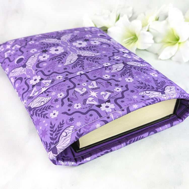 Purple book sleeve featuring a celestial moth and floral design with moons, stars, vines, and blossoms in soft lavender and violet shades.