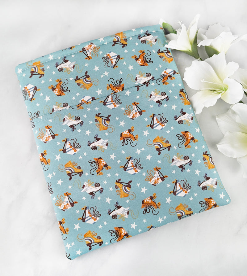 large padded book sleeve with pocket. fabric showcases orange and white roller blades and tiny white stars on a dusty blue background.