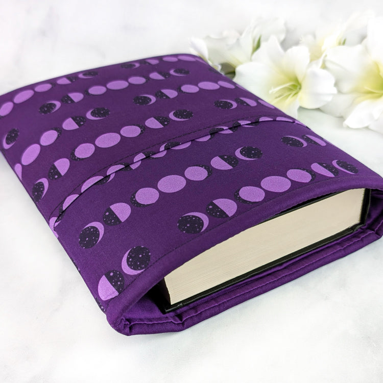 Deep purple book sleeve featuring a repeating moon phase pattern in lavender and black, creating a bold celestial design.