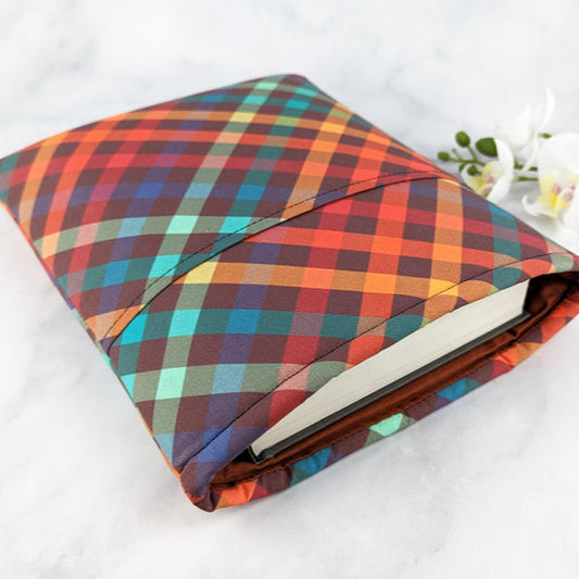 large padded book sleeve with pocket,  fabric pattern features bold plaid pattern in shades of red, brown, orange, teal and green.