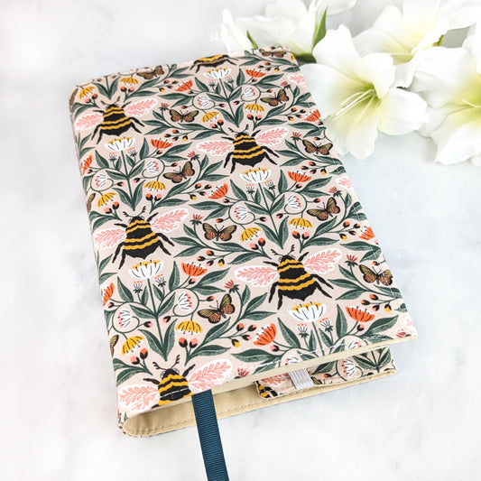 Beige book cover with a charming bee and butterfly pattern surrounded by pink, white, and yellow wildflowers on leafy green vines.