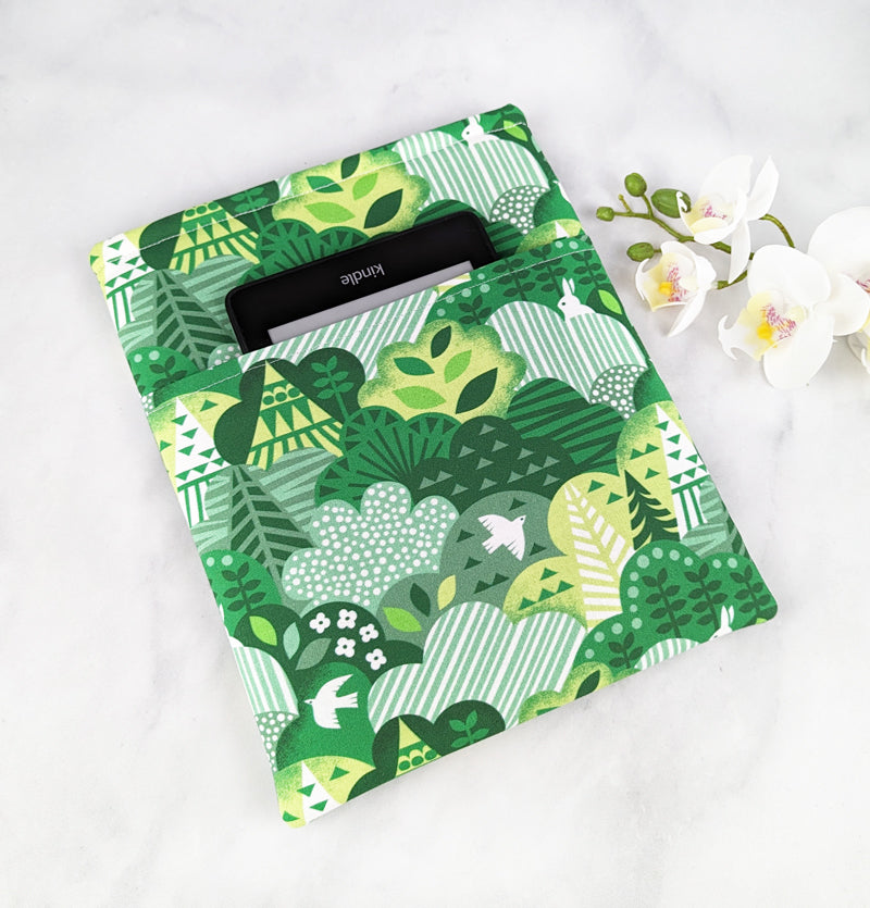 medium padded book sleeve with pocket. fabric showcases whimsical foresty hills with white birds and rabbits hidden throughout.