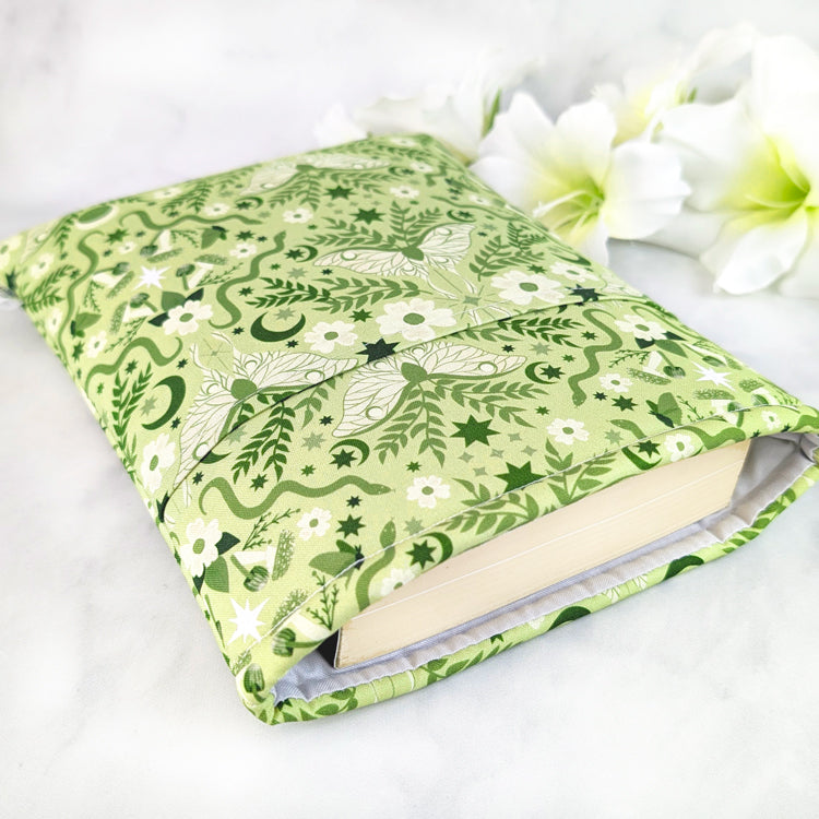 Light green book sleeve with white moths, moons, stars, and floral vines in a whimsical celestial pattern.
