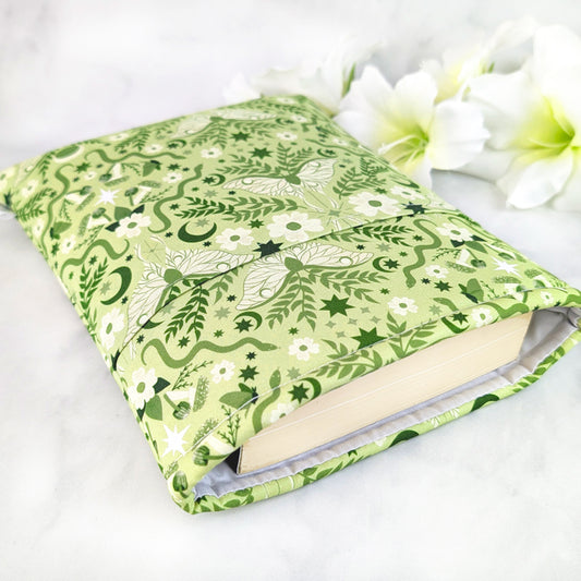 Light green book sleeve with white moths, moons, stars, and floral vines in a whimsical celestial pattern.