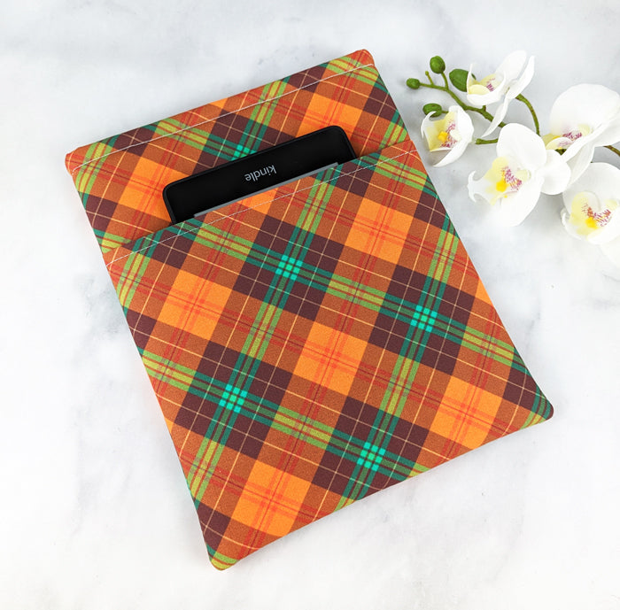 medium padded book sleeve with pocket. fabric features plaid pattern in shades of orange, green and brown.