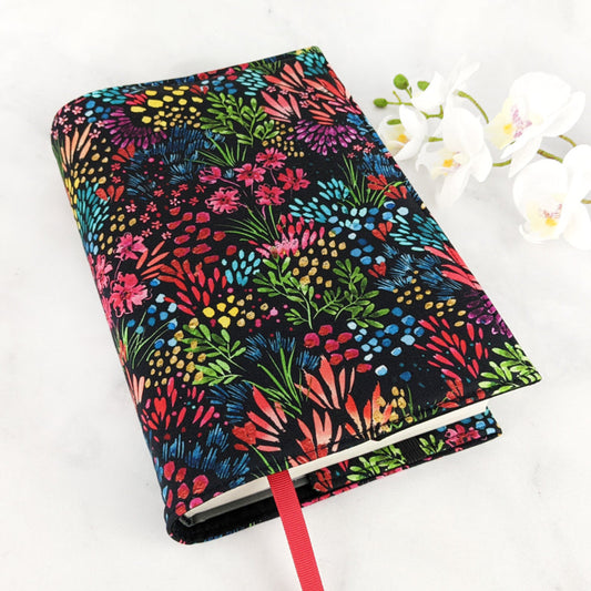 Fabric book cover with a vibrant botanical print featuring multicolored flowers and foliage in neon-like hues against a deep black background, finished with a bold red ribbon bookmark.