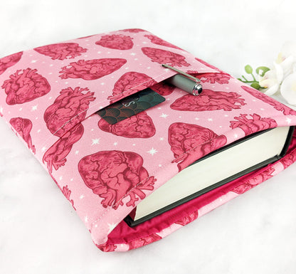 A pink fabric book sleeve featuring a repeating pattern of red anatomical hearts and white stars.