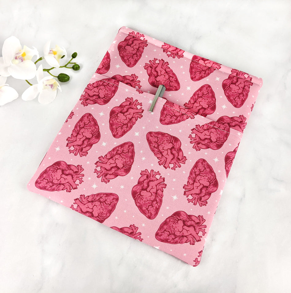 A pink fabric book sleeve featuring a repeating pattern of red anatomical hearts and white stars.