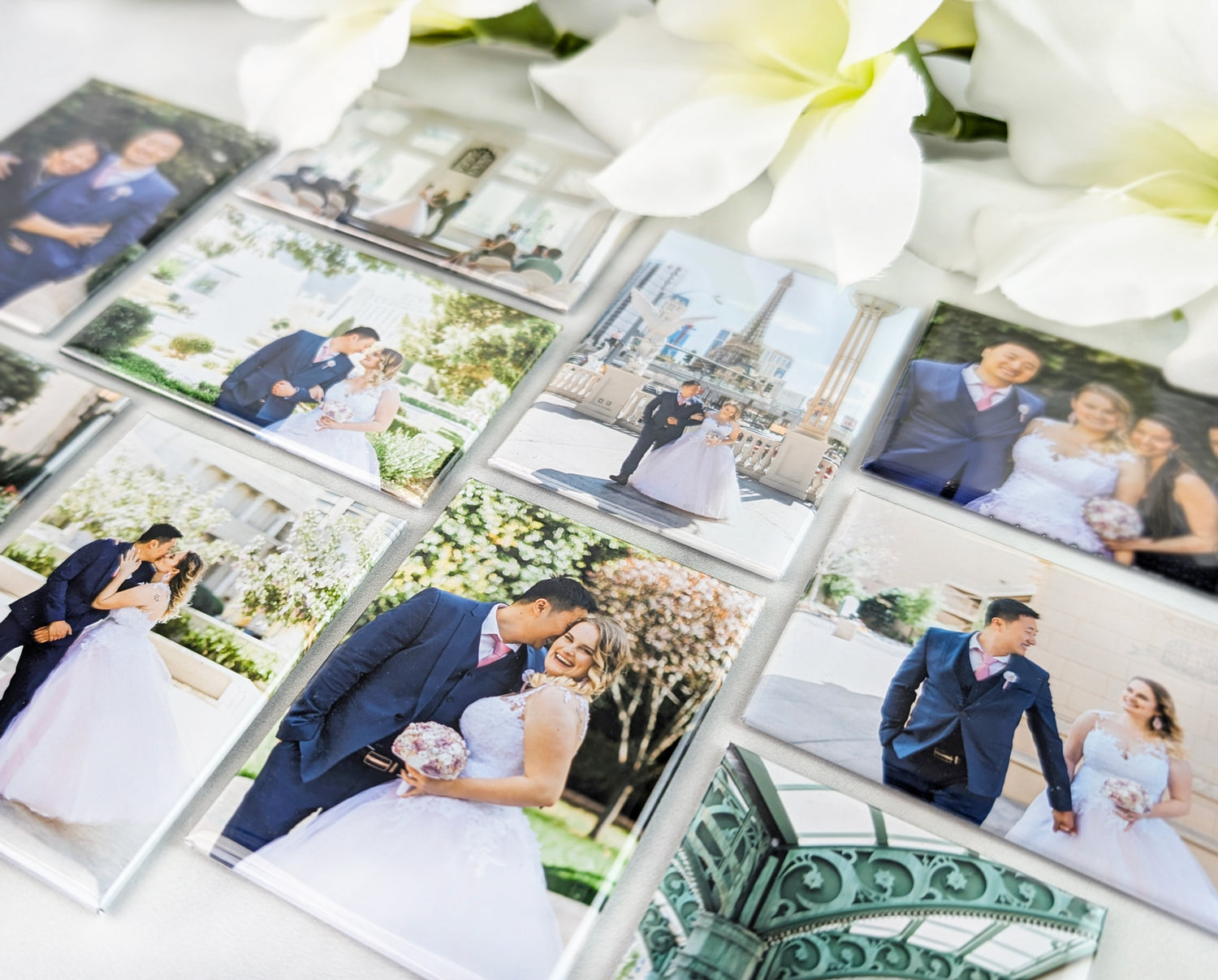 A set of rectangular photo magnets displayed on a light surface, each featuring vibrant wedding portraits of a couple in various romantic poses. The magnets are arranged in a grid and surrounded by white flowers, showcasing the clarity and full-color print quality.