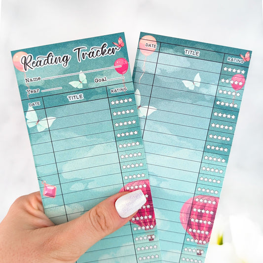 Two teal fantasy-themed reading tracker bookmarks with balloon and butterfly accents, held in a hand with silver nail polish.