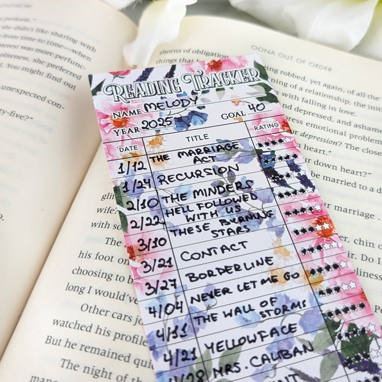 Colorful floral reading tracker bookmark filled with handwritten book titles and star ratings, resting on an open book.