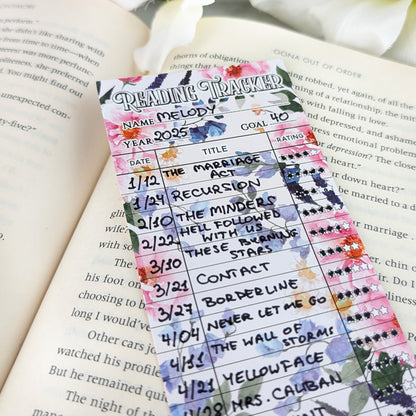 Colorful floral reading tracker bookmark filled with handwritten book titles and star ratings, resting on an open book.
