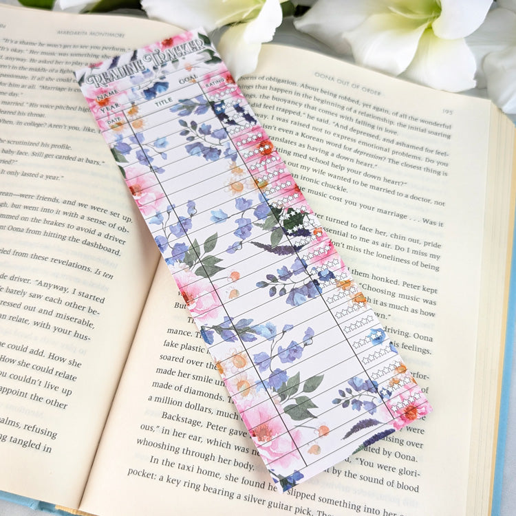 Blank floral reading tracker bookmark with pink, blue, and orange flowers, placed on an open book.