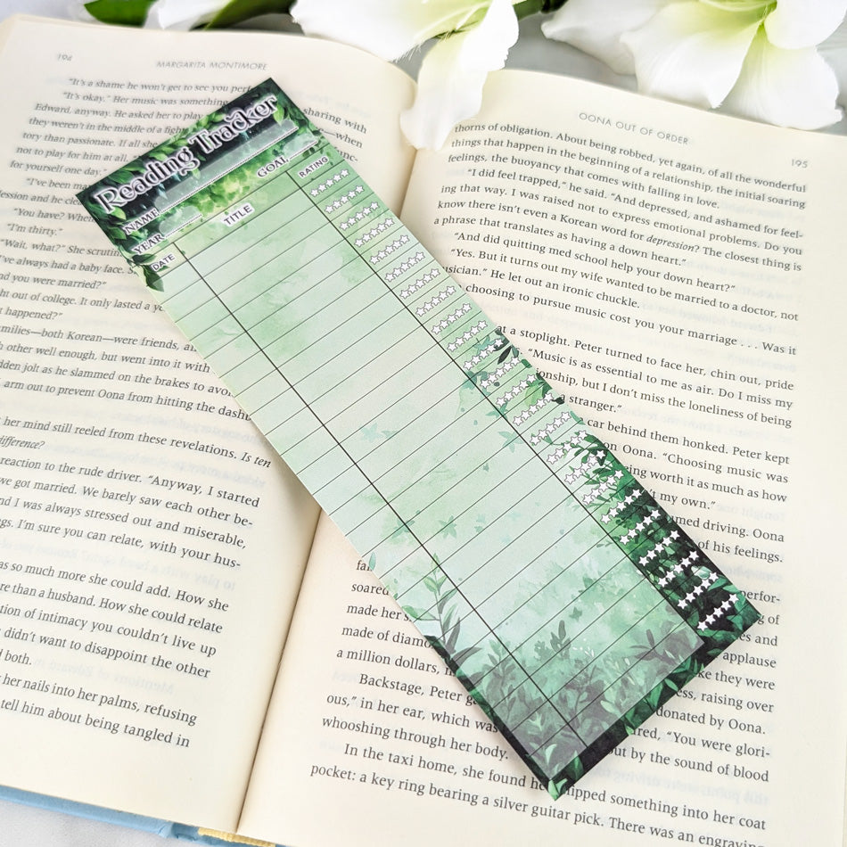 Blank green reading tracker bookmark with leafy border design, placed on an open book.