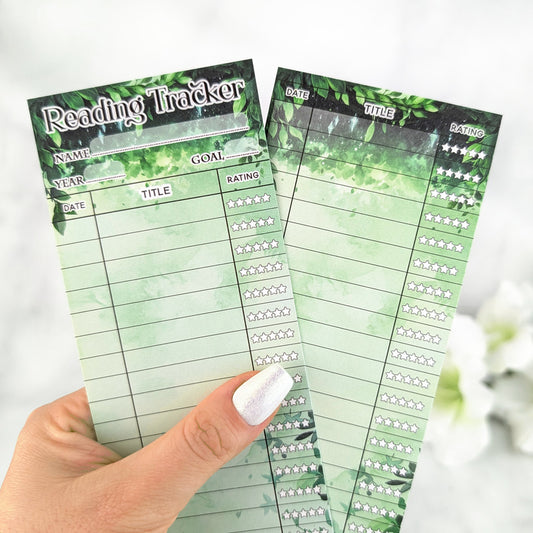 Two green leafy reading tracker bookmarks with gradient backgrounds, held in a hand with silver nail polish.
