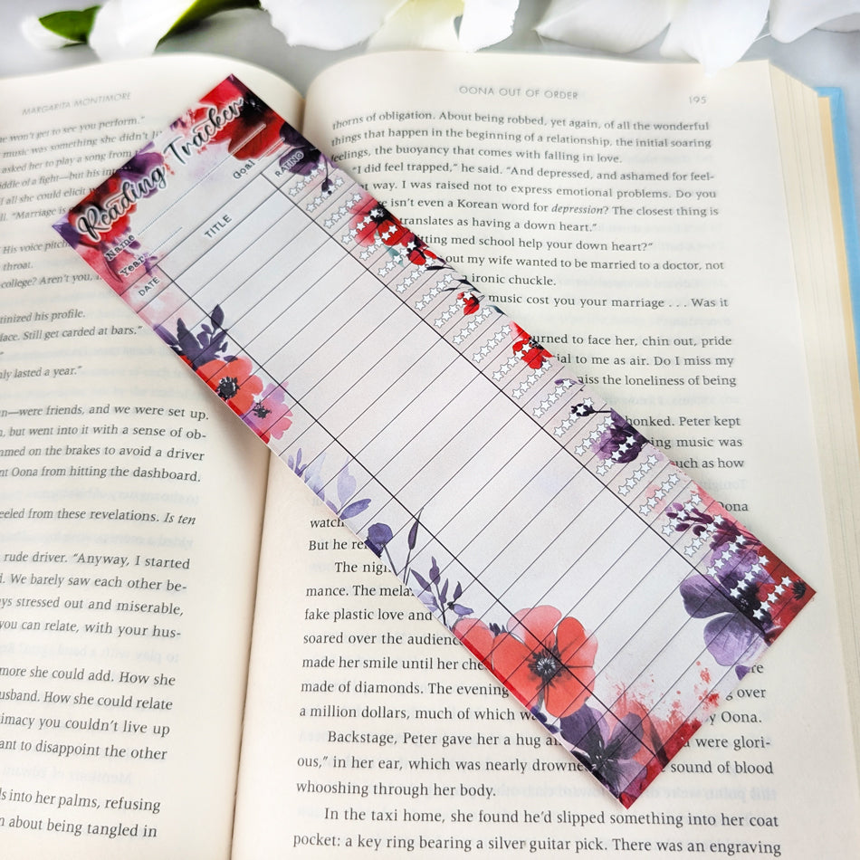 Red and purple floral reading tracker bookmark with blank spaces for dates, titles, and ratings, placed on an open book.