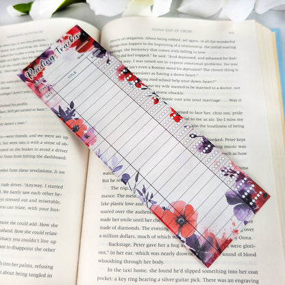 Red and purple floral reading tracker bookmark with blank spaces for dates, titles, and ratings, placed on an open book.
