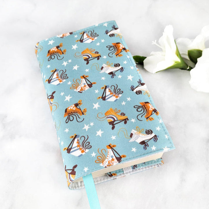 small adjustable book cover, fabric showcases orange and white roller blades and tiny white stars on a dusty blue background.