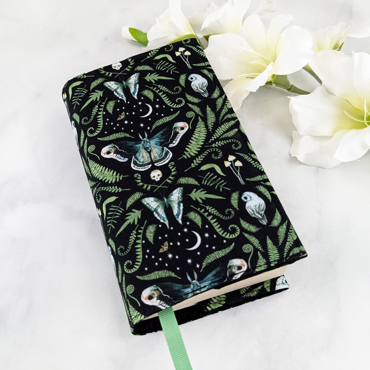 adjustable fabric book cover, fabric pattern featuring ferns, moths, mushrooms, owls and skulls on a black background.