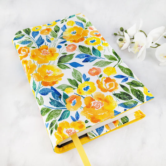 Fabric book cover with a cheerful floral print in shades of yellow, orange, and blue on a white background, finished with a yellow ribbon bookmark.
