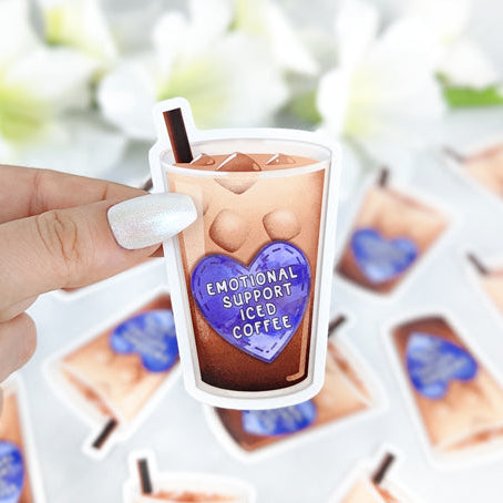 hand holding a vinyl sticker. Sticker shows a drawing of glass of iced coffee with a purple heart patch with words Emotional Support Iced Coffee.