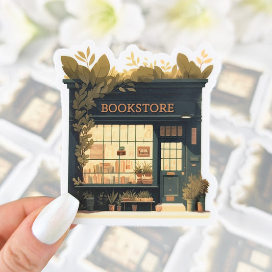 Vinyl sticker of a cozy green bookstore with plants around the entrance and books displayed in the window, held by a hand with iridescent white nail polish.
