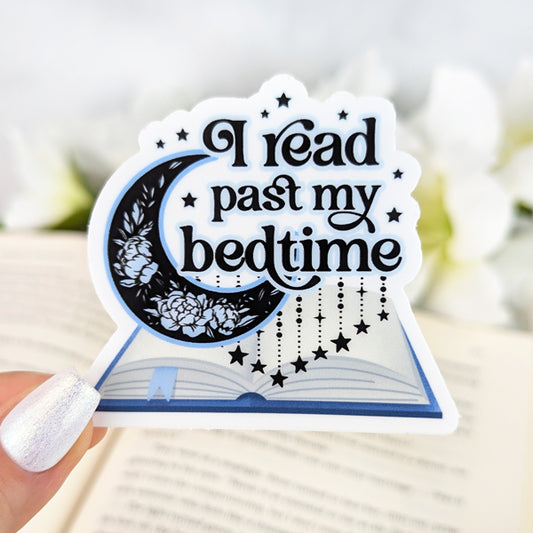 Vinyl sticker with the phrase “I read past my bedtime,” featuring a crescent moon with floral details, hanging stars, and an open book design, held by a hand with iridescent white nail polish.