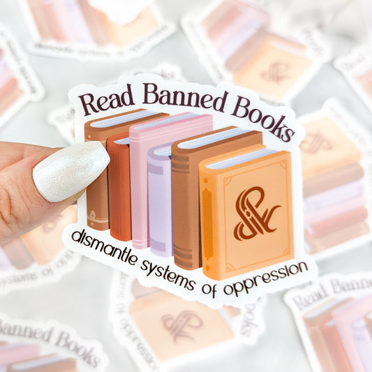 vinyl sticker with illustrated books in warm tones and the text “Read Banned Books – dismantle systems of oppression,” held by a hand with iridescent white nail polish.