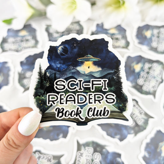 Vinyl sticker featuring a night sky with UFO, mountains, and planets, with the text “Sci-Fi Readers Book Club,” held by a hand with iridescent white nail polish.