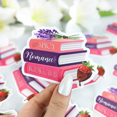 Vinyl sticker of stacked pink and purple books with lavender sprigs and a chocolate-covered strawberry, labeled “Spicy Romance Book Club,” held by a hand with iridescent white nail polish.