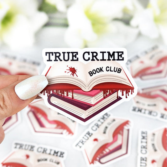 sticker featuring a stack of books with dripping blood and the text "True Crime Book Club" in a spooky style held by a hand with light nail polish. More identical stickers are scattered in the background.